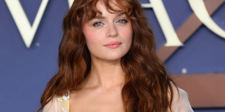 Joey King poses on the red carpet at the “Practical Magic 2” premiere with curly, wispy “Wicked Bangs” and long auburn waves.